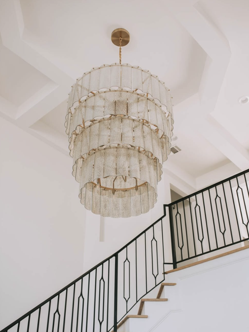 Tiered mesh chandelier hanging in a two-story foyer with iron staircase railing, white walls, and high ceiling