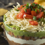 7-Layered Mexican Dip Appetizer; refried beans mixture, sour cream, salsa, guacamole, cheese, tomatoes, and green onions!