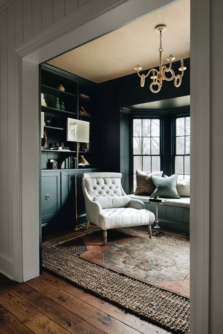 Dark moody home library with tufted armchair, built-in shelves, and window seat