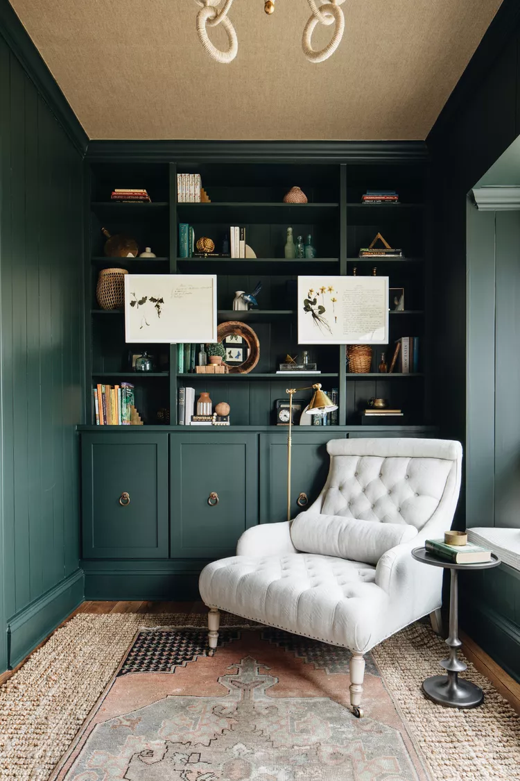 Dark green built-in bookshelves with tufted white armchair and brass accents