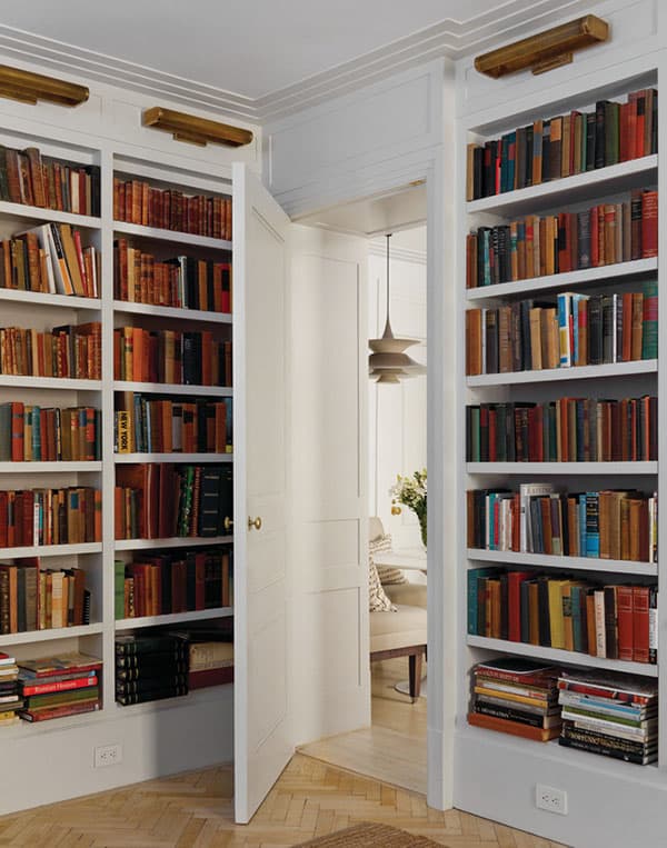 Built-in white bookshelves with a hidden door leading to a cozy home office space