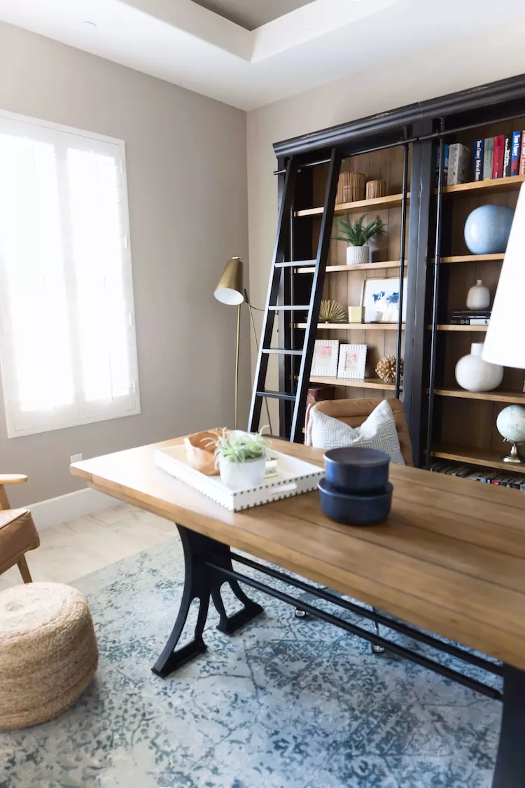 Modern home office with large wooden desk, ladder bookshelves, and styled decor