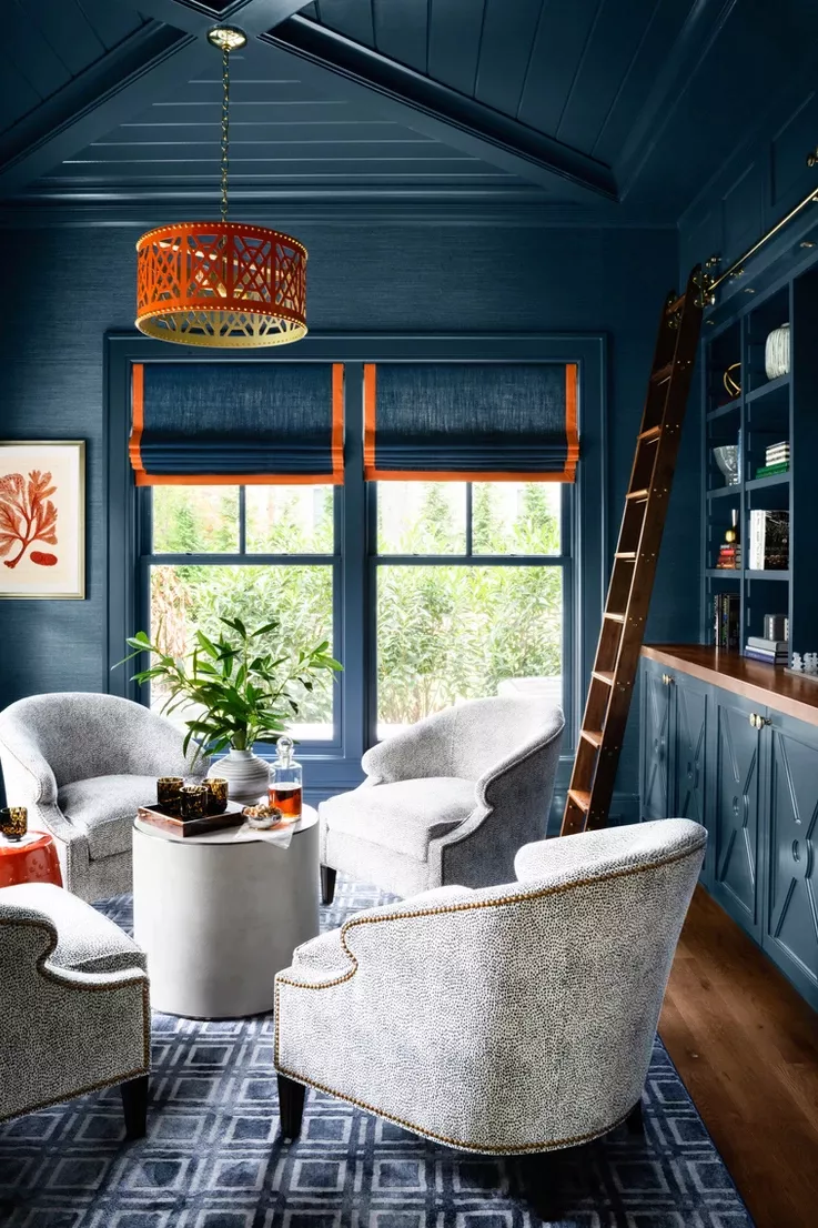 Navy blue home library with built-in shelves, ladder, and cozy seating area