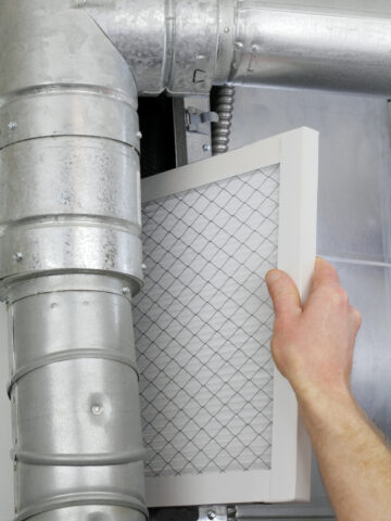 A man's arm and hand seen replacing disposable air filter in home central air furnace. - How to Make Your Home More Comfortable With the Right Air Filter