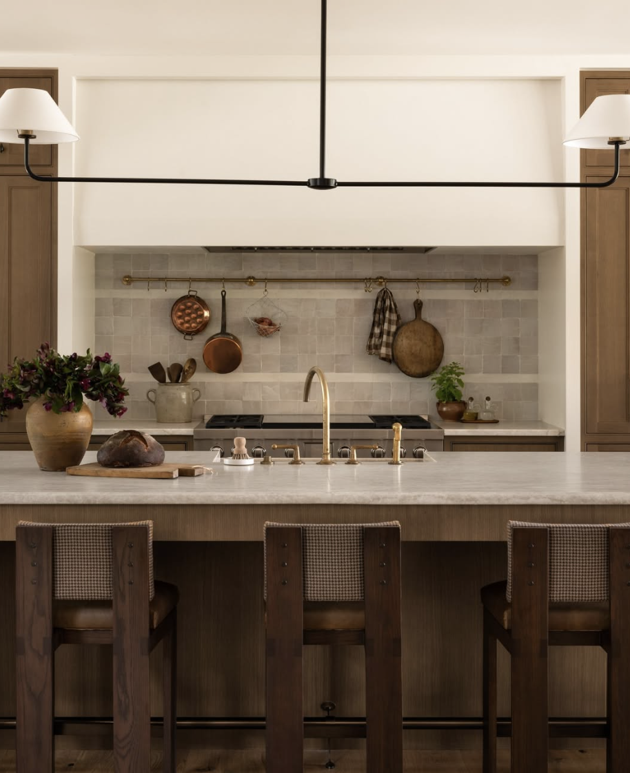 European-inspired kitchen with a square tile backsplash, brass rail system, warm wood cabinetry, and vintage cookware accents.