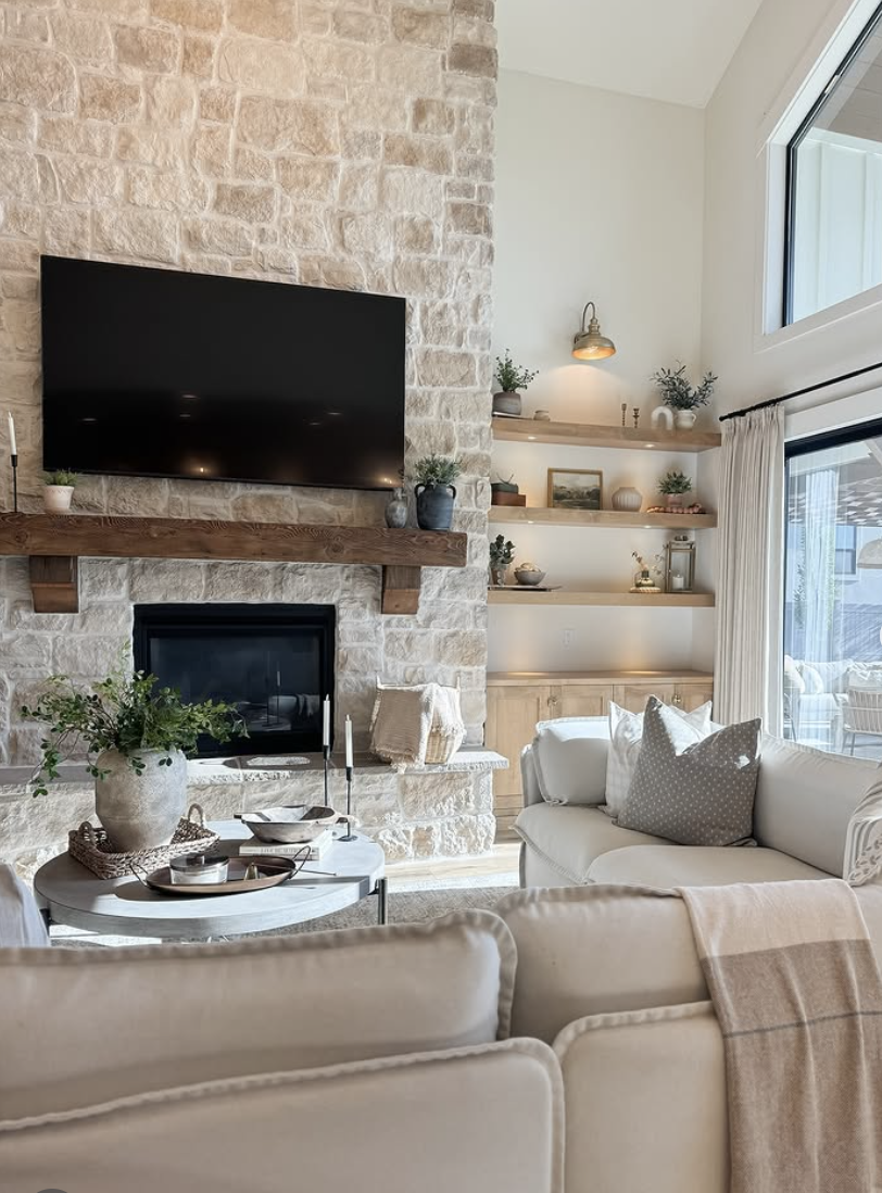 Farmhouse living room with stone fireplace, mounted TV above wood mantel, and floating wood shelves