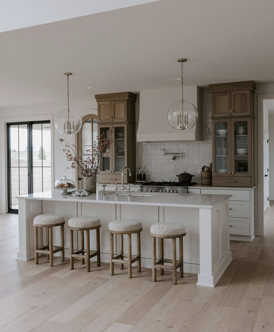 Farmhouse kitchen with a full-height zellige tile backsplash, custom range hood, warm wood cabinetry, and a large white island.