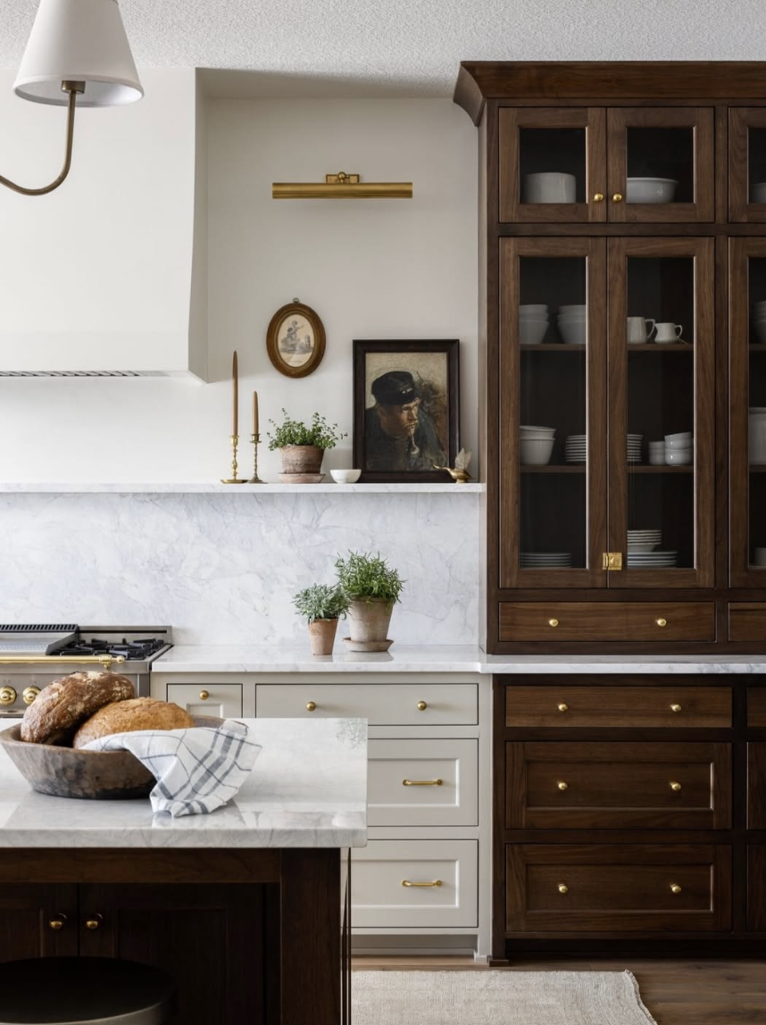 Kitchen with a full-height marble slab backsplash, warm wood cabinetry, brass hardware, and a classic plaster range hood for a timeless farmhouse look.