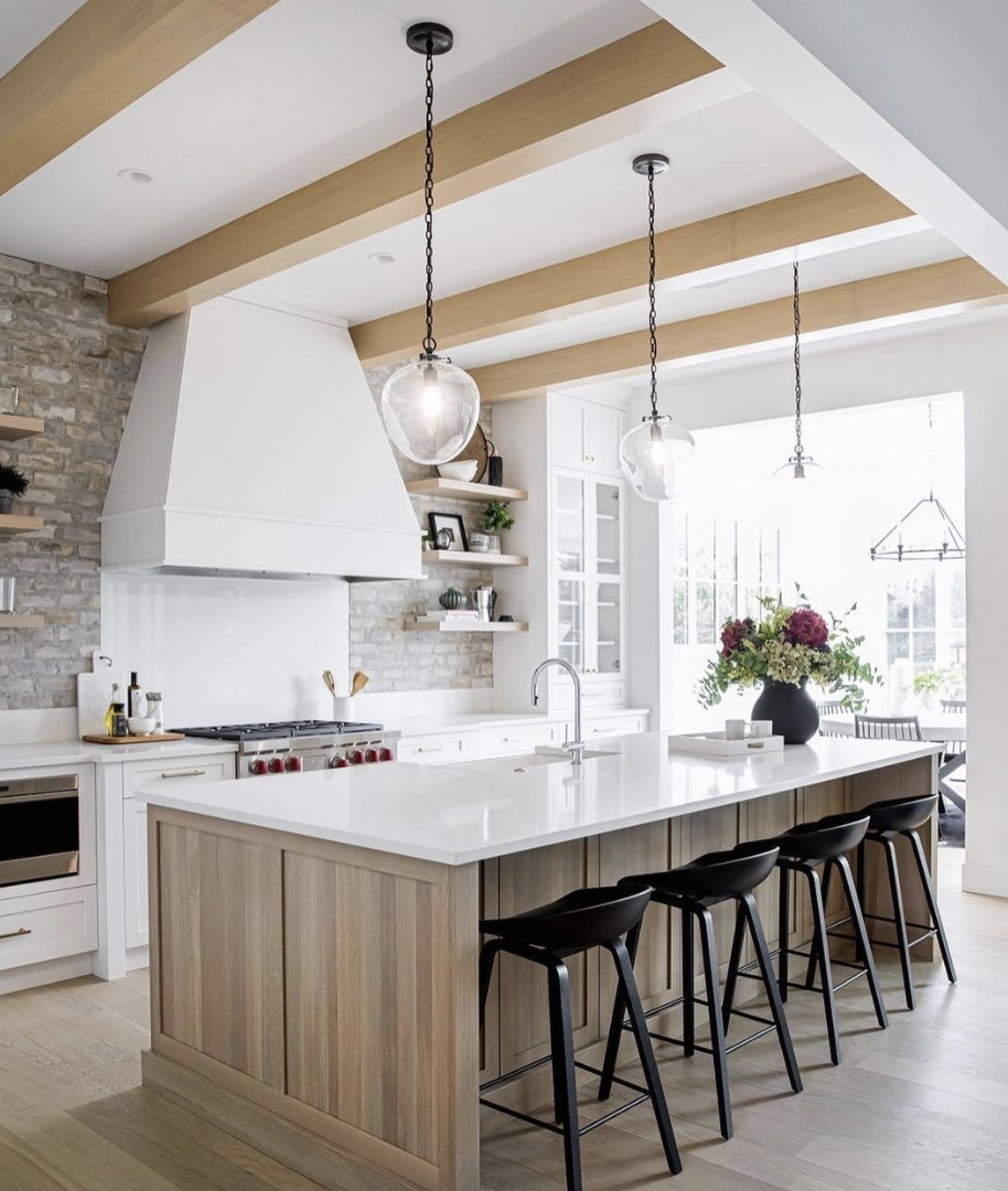 Kitchen with a mixed material backsplash featuring stone, a plaster range hood, and wood shelving in a modern farmhouse design.