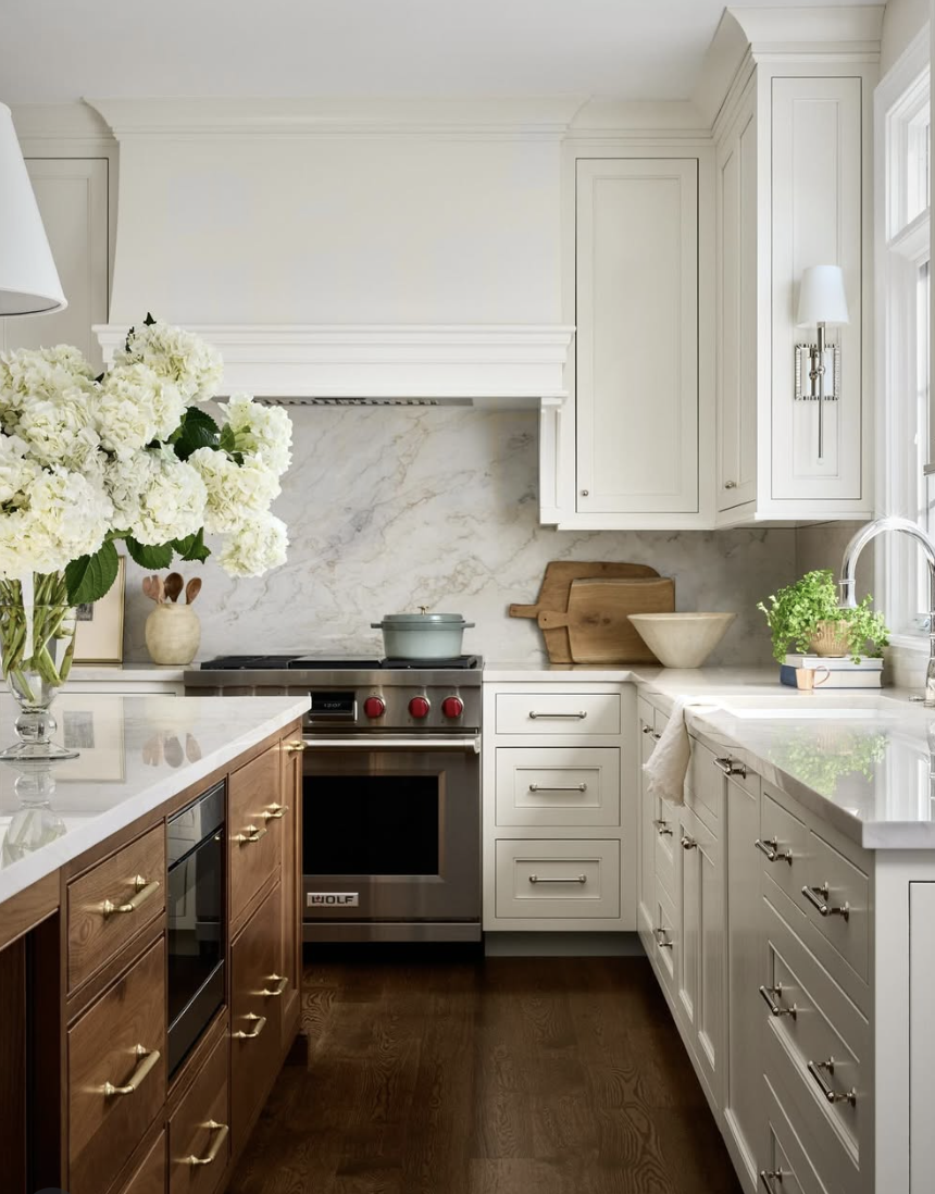 Statement range hood with a marble slab backsplash framed behind the cooktop in a classic farmhouse kitchen.