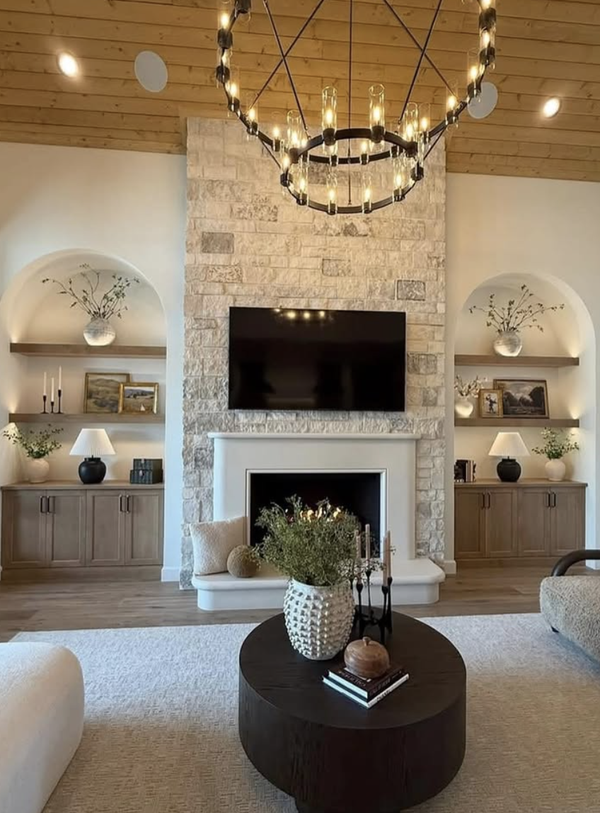 Living room with stone fireplace wall, mounted TV above mantel, arched built-in shelves, and wood ceiling