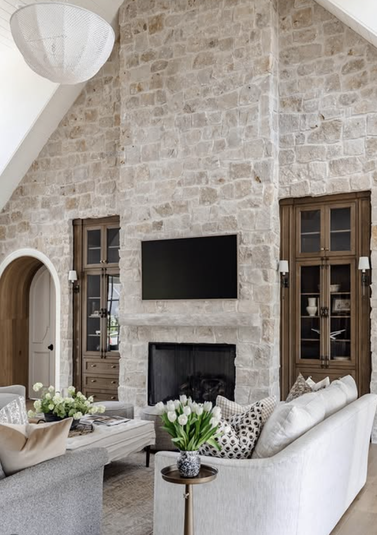 Living room with tall stone fireplace, mounted TV above mantel, and built-in wood cabinets on each side