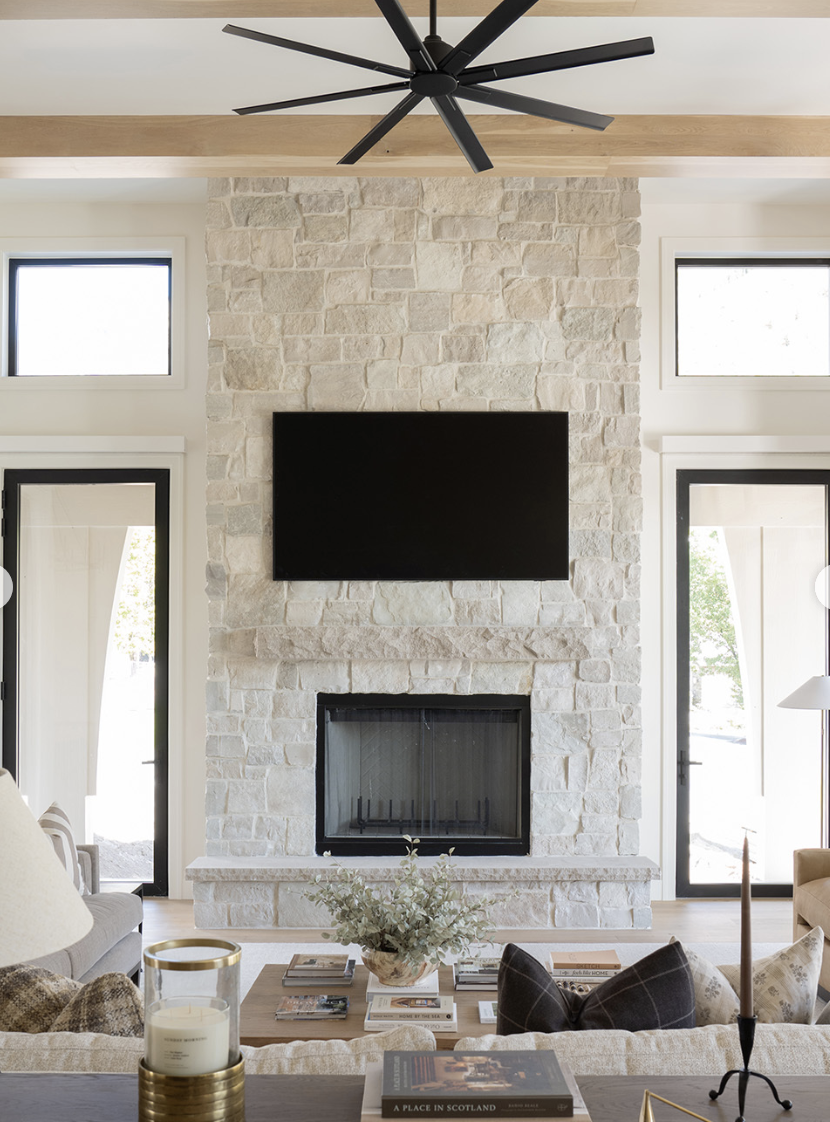 Living room with tall stone fireplace, mounted TV above mantel, high ceilings, and black-framed glass doors