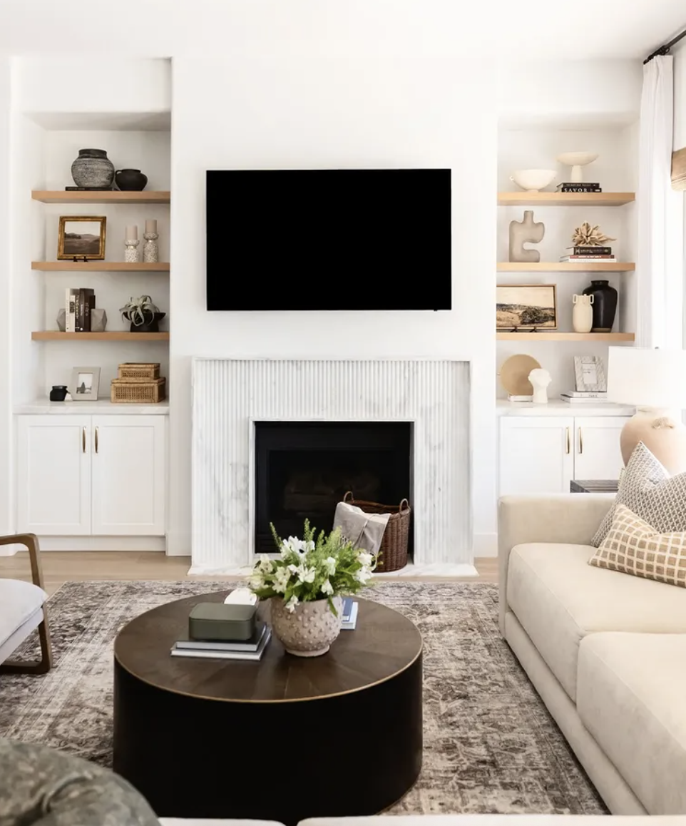 White living room fireplace with mounted TV, vertical textured surround, and floating wood shelves on both sides