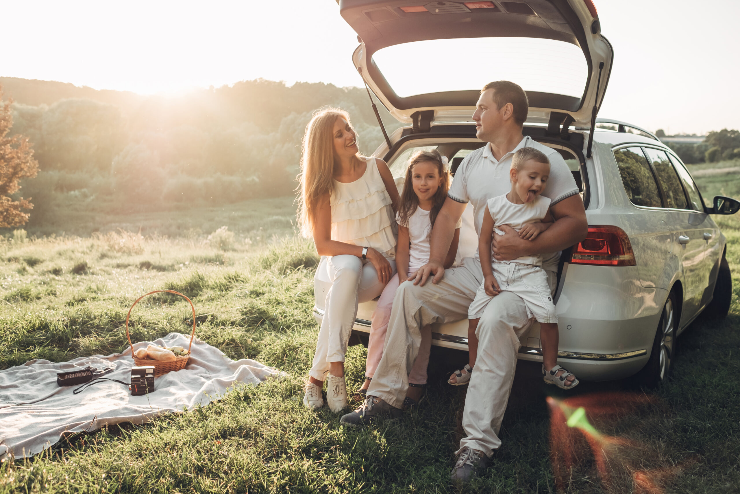 How To Prep Your Child for a Trip With a Family Friend - Adult couple with their little children having picnic in the Park Outside the City, Family Weekend Concept, Four People Enjoying Summer