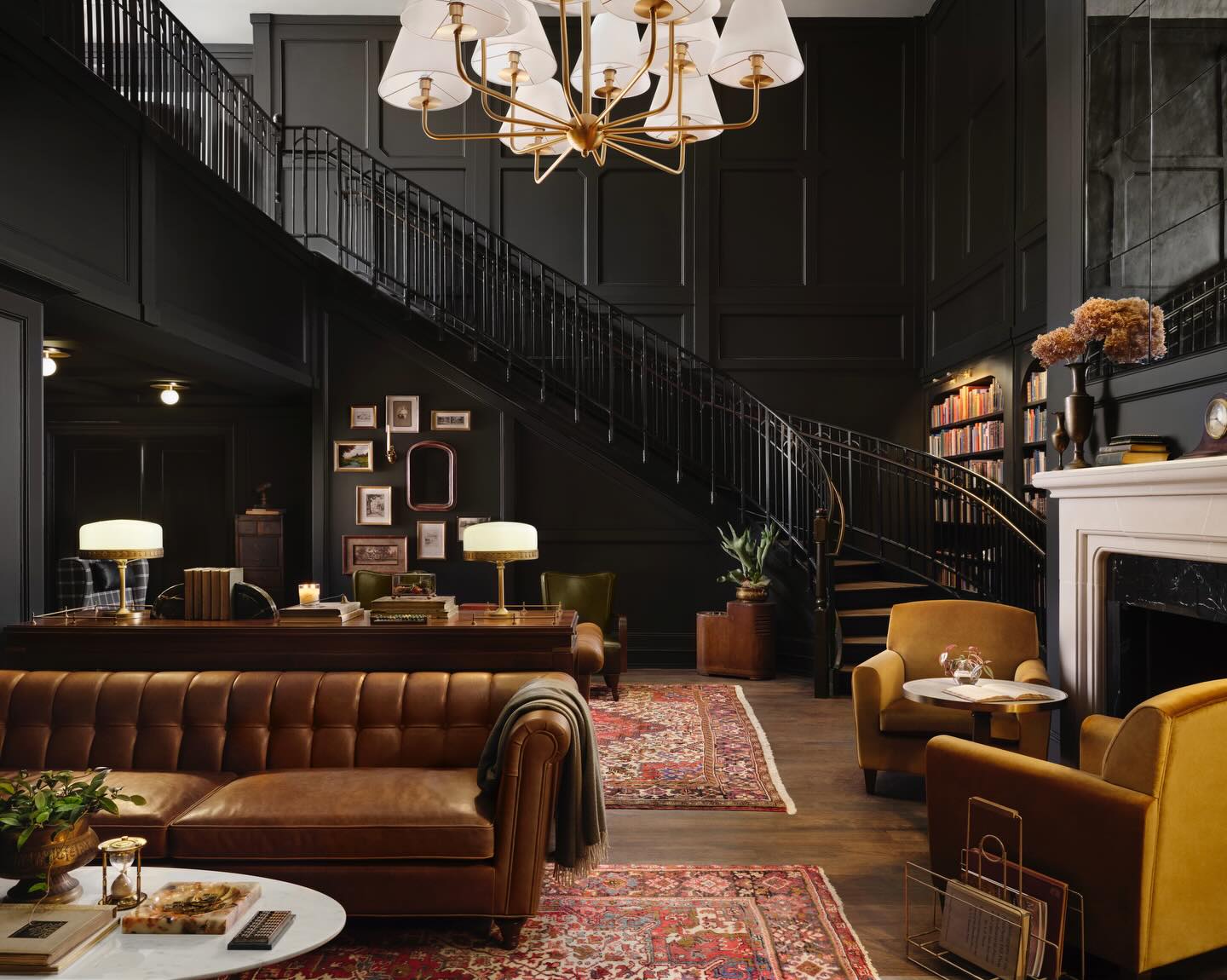 Black living room by Joanna Gaines featuring a curved staircase, paneled walls, leather sofa, vintage rugs, and a classic fireplace.