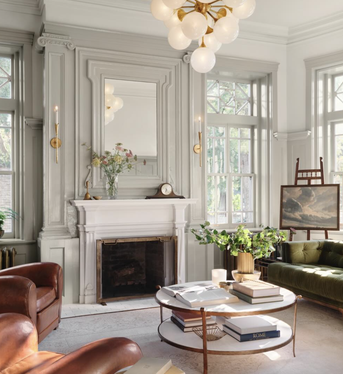 Light gray living room by Joanna Gaines featuring classic wall molding, an elegant fireplace, brass lighting, and soft neutral seating.