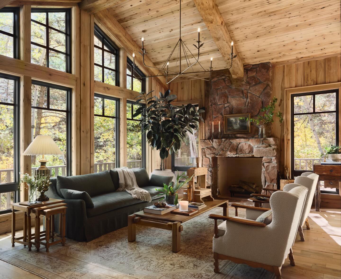 Rustic living room by Joanna Gaines featuring exposed wood beams, large windows, a stone fireplace, and cozy farmhouse seating.