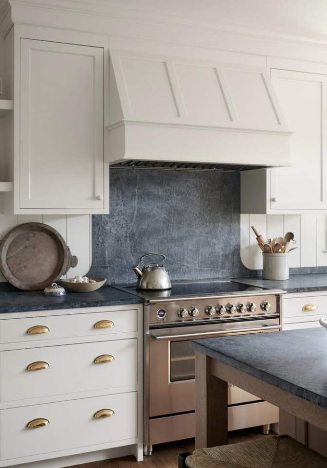 White cabinets with black countertops and brass hardware in a timeless kitchen with a statement range and backsplash