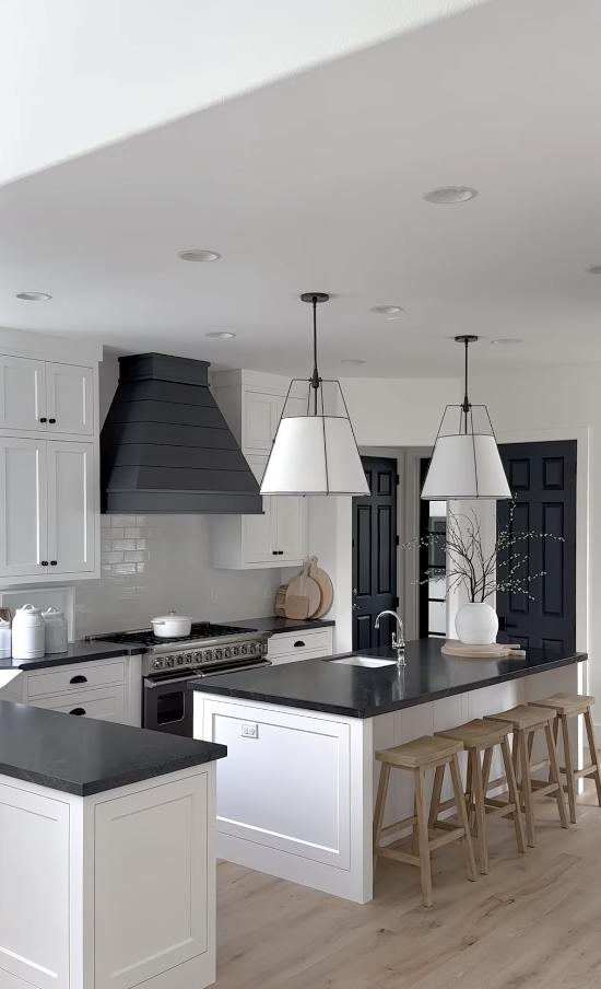 White cabinets with black countertops in a bright farmhouse kitchen featuring a large island and black range hood