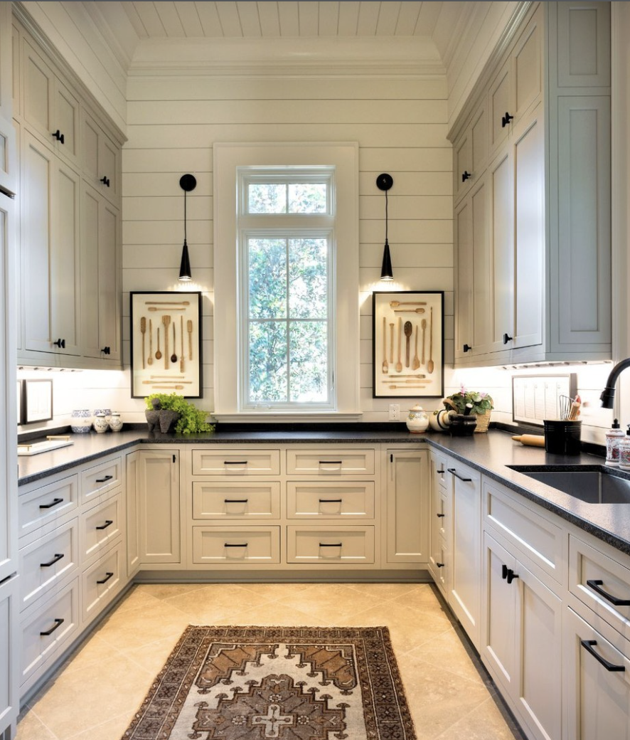 White cabinets with black countertops in a bright kitchen featuring shiplap walls and matte black hardware