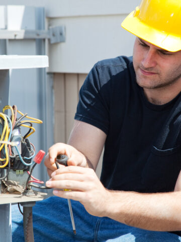 Young repairman fixing an industrial air conditioning compressor. - Why is Professional AC Installation Important?