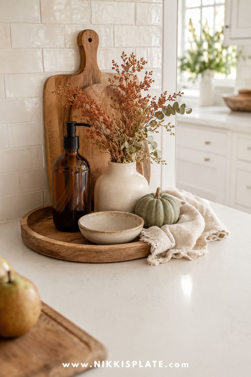 Fall kitchen counter decor arranged on a wood tray with an amber soap bottle, cream vase, dried rust stems, sage pumpkin and folded flax linen.