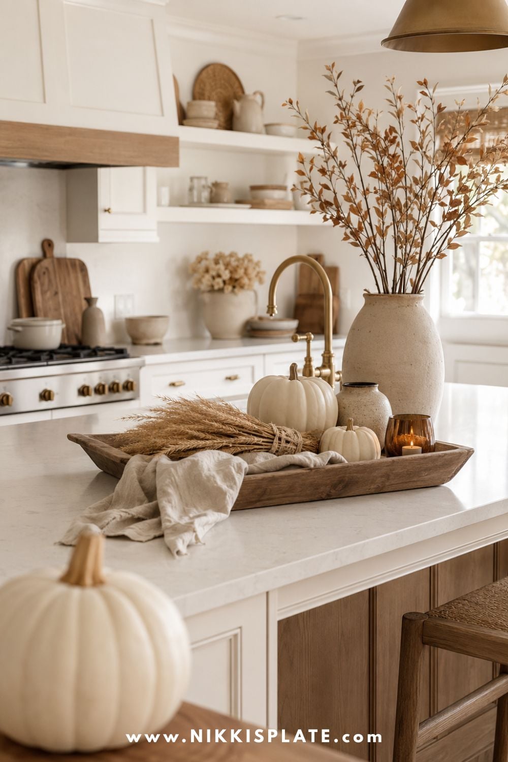 Neutral fall kitchen decor with cream pumpkins, taupe pottery, oatmeal linen, wheat, warm wood, soft brown branches and aged brass on a light island.