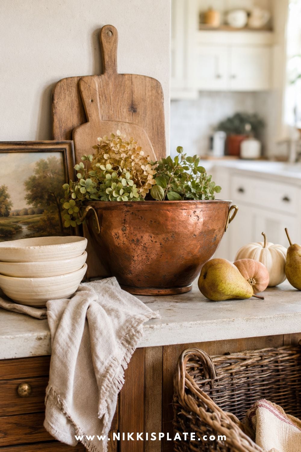 Thrifted fall kitchen decor featuring a patinated copper bowl, warm wood cutting boards, cream dishes, vintage landscape art, pears and natural linen.