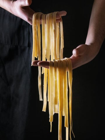 Culinary Escapades - Fresh raw uncooked homemade pasta tagliatelle in man's hands over black apron as background.