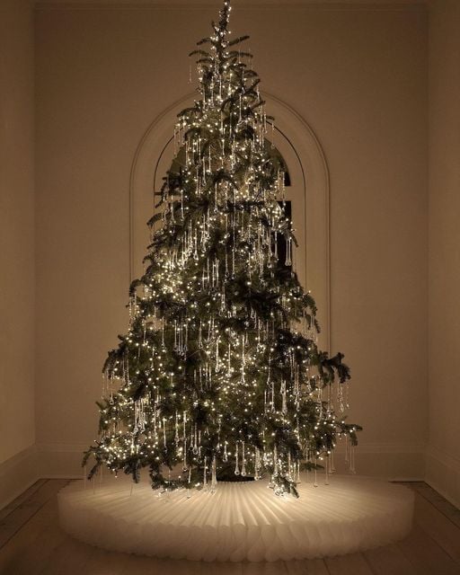 Elegant minimalist tinsel Christmas tree with cascading silver tinsel and warm white lights in a neutral room with a soft white tree skirt.
