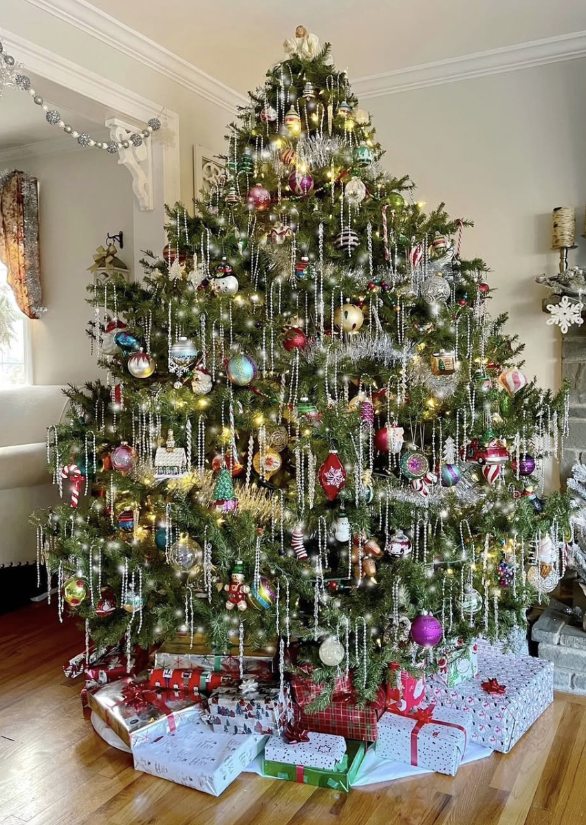Classic family tinsel Christmas tree decorated with colorful ornaments, silver tinsel, and glowing lights surrounded by wrapped presents on hardwood floors.