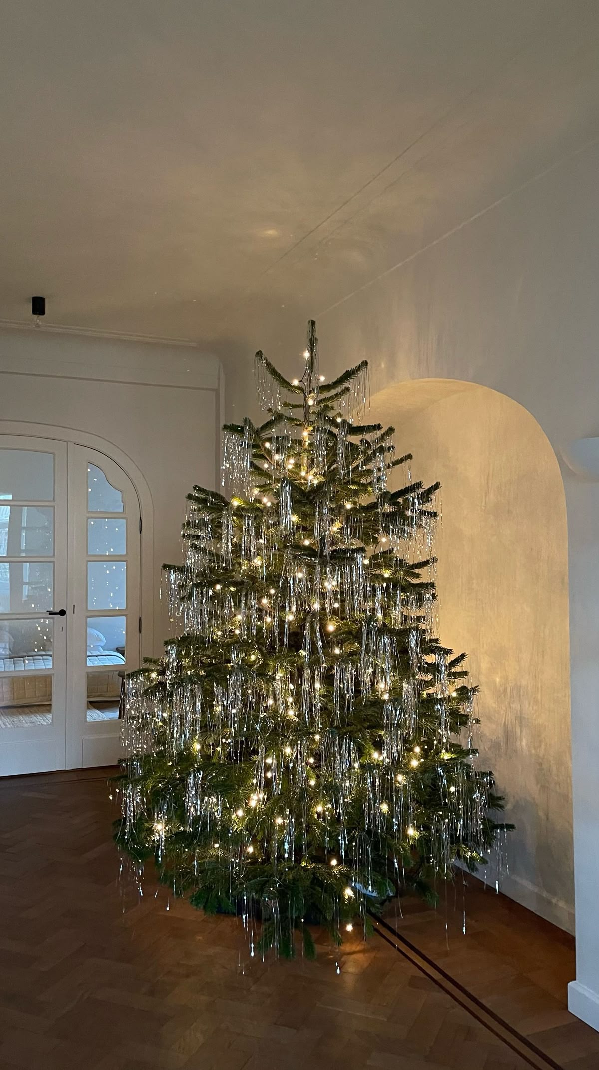 Scandinavian minimalist tinsel Christmas tree decorated with silver tinsel and warm white lights in a cozy neutral living room.