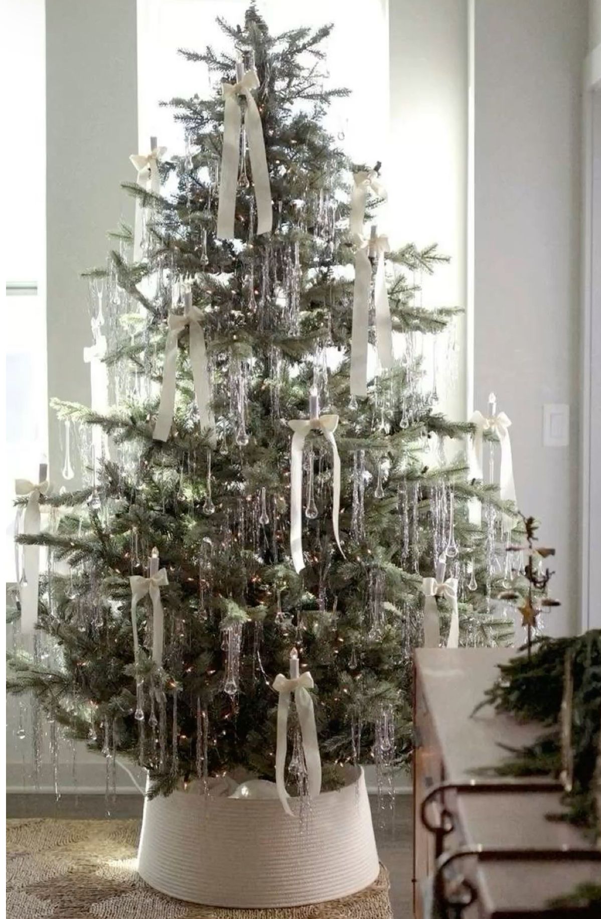 White ribbon tinsel Christmas tree with silver tinsel and ivory bows in a bright, neutral living room with natural light.