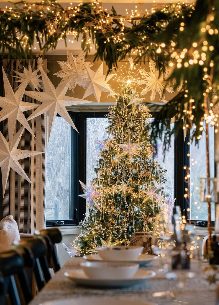 Winter Wonderland tinsel Christmas tree decorated with silver tinsel, glowing lights, and paper star decorations in a cozy dining room setting.