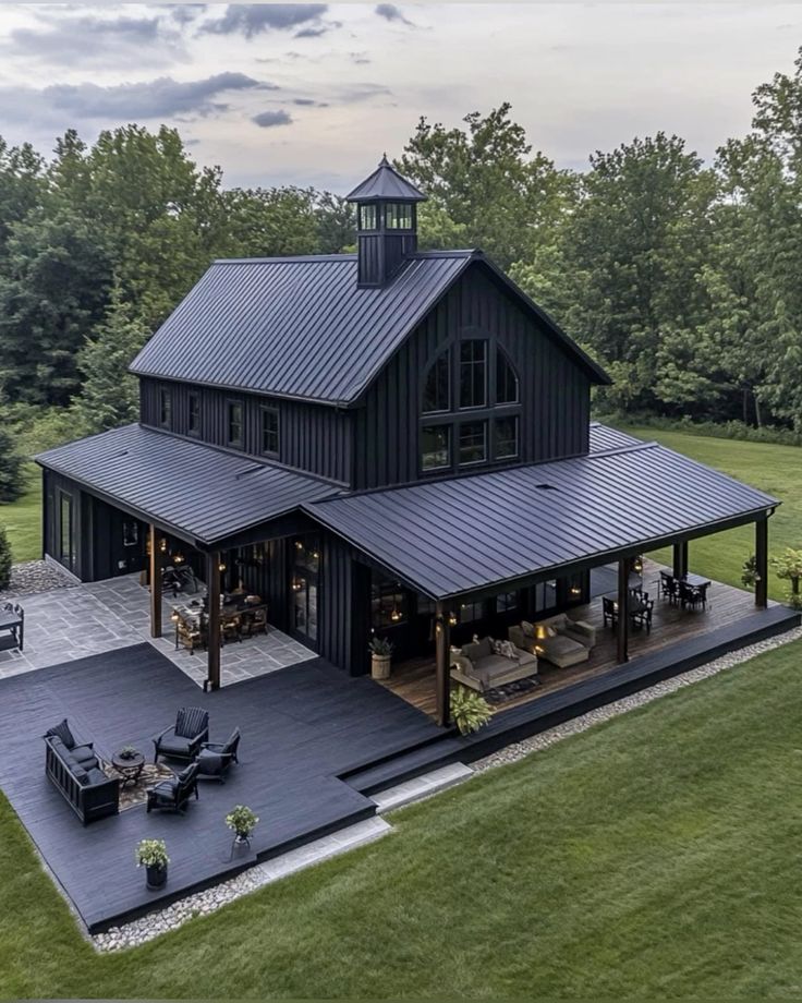 This luxury black barndominium is the definition of modern farmhouse elegance. Its wraparound covered patio and open deck create endless space for entertaining and relaxing outdoors. The deep black exterior, metal roofing, and large windows give the home a bold, upscale presence, while warm lighting and natural wood accents keep it cozy and inviting.