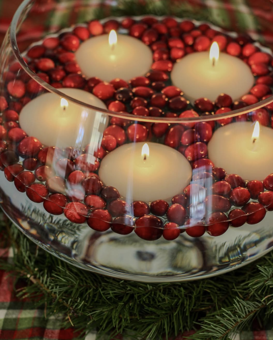 Large glass bowl filled with water, cranberries, and floating candles surrounded by greenery for a warm and festive Christmas centerpiece.