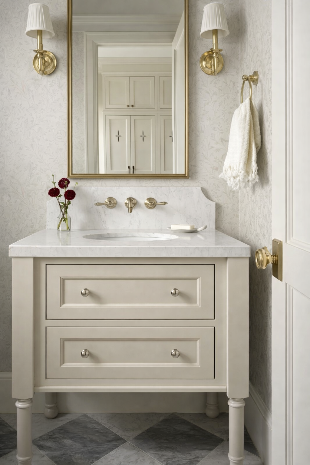 Furniture-style vanity in a powder bathroom with soft neutral wallpaper, cream cabinetry, marble countertop, and brass sconces creating a warm, modern farmhouse look for 2026.