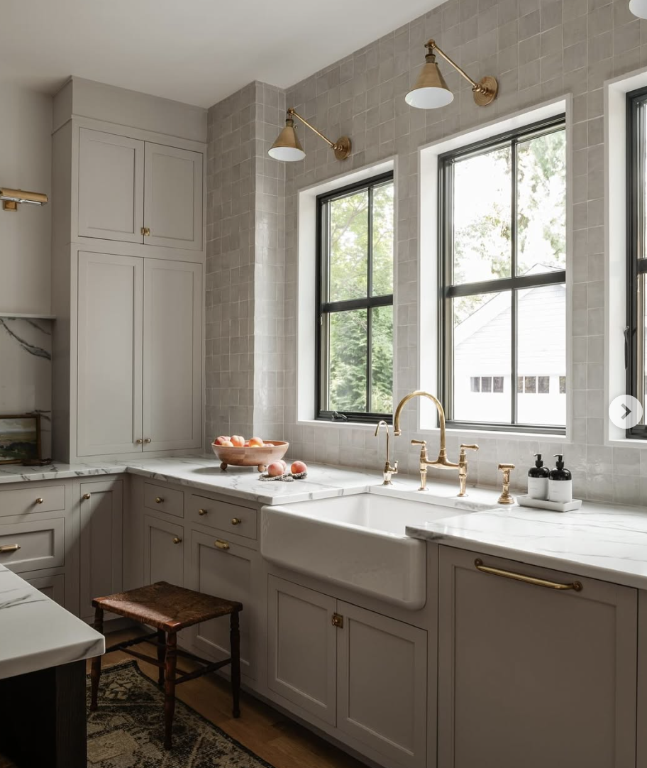 Oversized farmhouse kitchen sink with marble countertops, brass fixtures, and soft neutral cabinetry showcasing a popular kitchen sink trend for 2026.