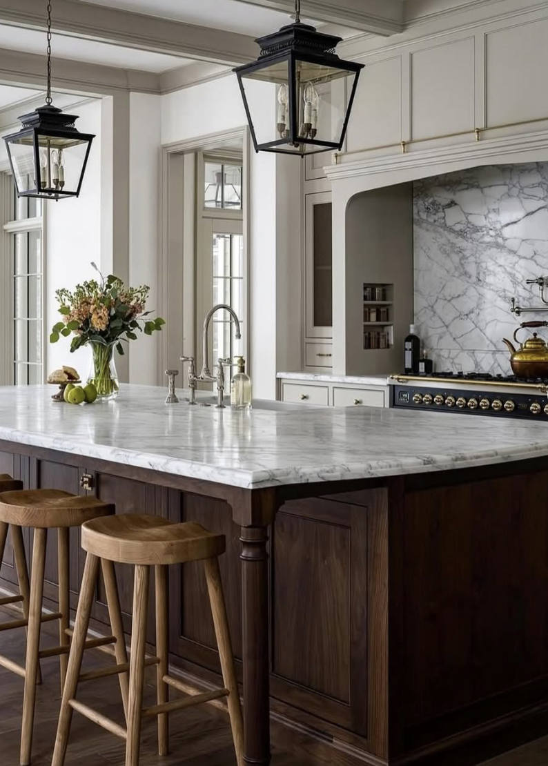 Two-tone kitchen with warm wood island and painted cabinetry, marble countertops, and brass hardware showcasing a popular kitchen trend for 2026.