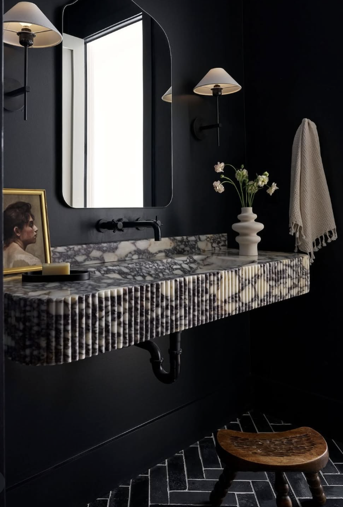 Black herringbone tile bathroom floor paired with a dark vanity, black walls, marble countertop, and soft ambient lighting.