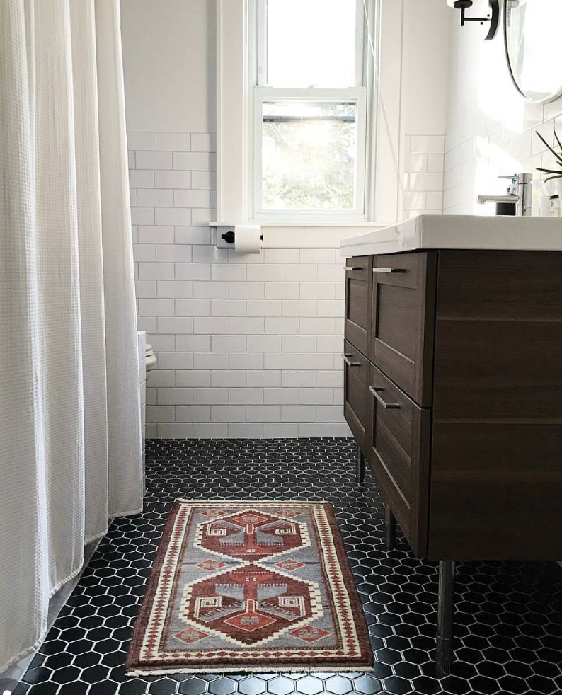 Black hexagon tile bathroom floor paired with white subway tile walls, a dark wood vanity, and natural light.