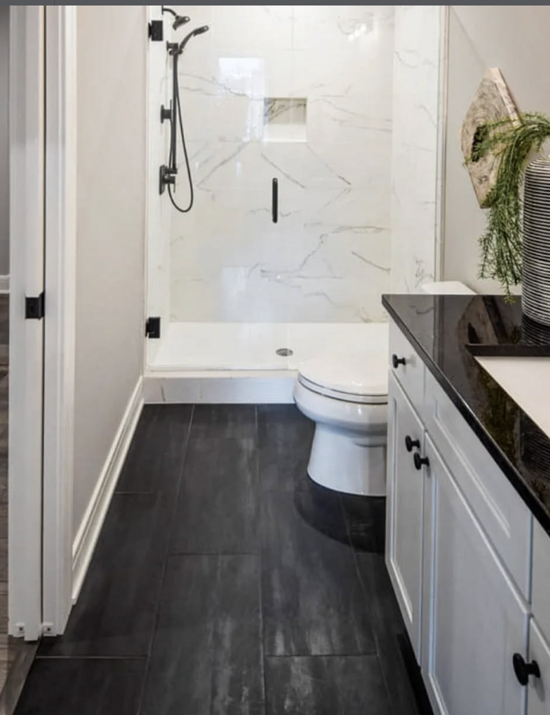 Black large format tile bathroom floor paired with a white vanity, black countertop, and a modern walk-in shower.