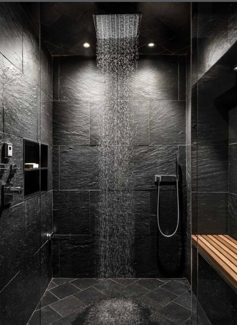 Black stone tile bathroom floor paired with dark stone shower walls, a rain shower head, and a built-in bench.