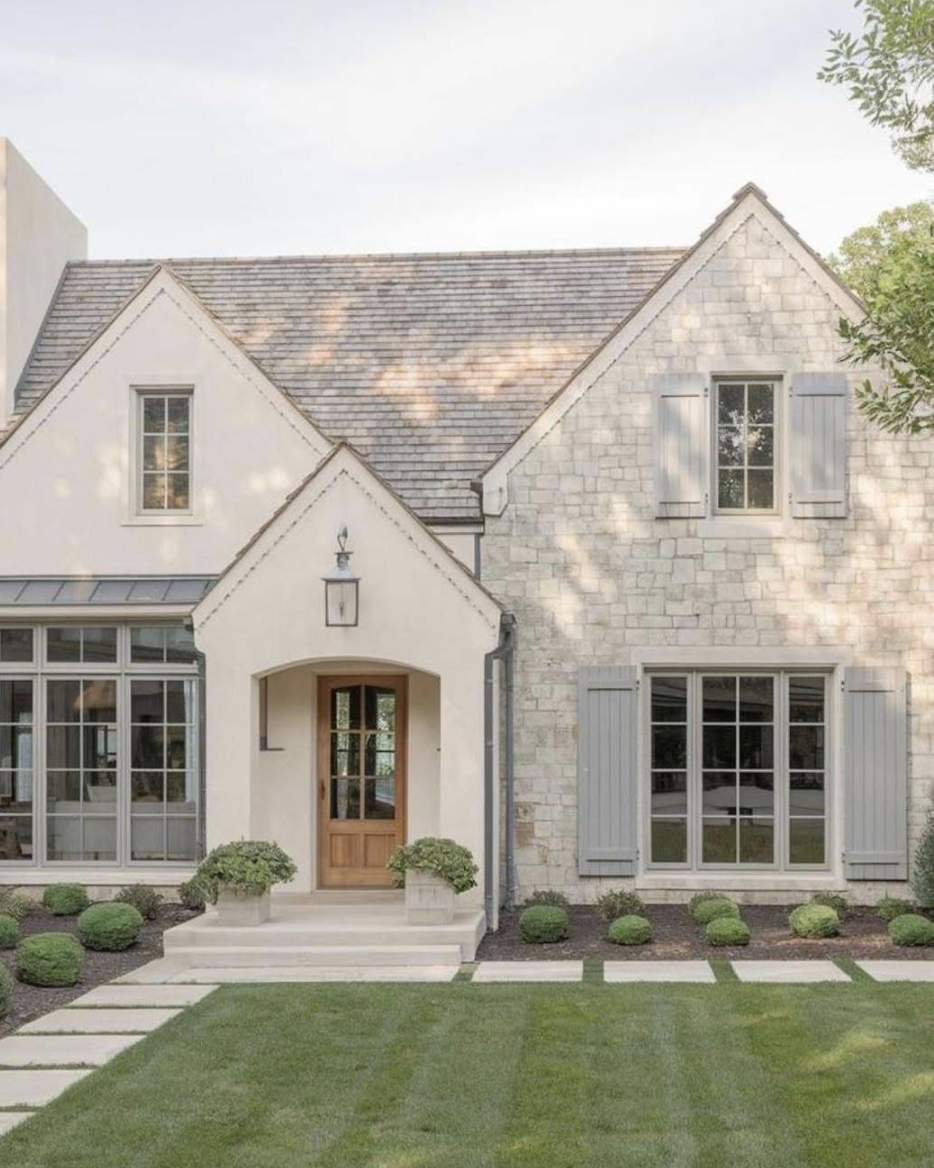 Warm neutral home exterior with light stone siding, soft cream stucco, and natural wood front door reflecting house exterior trends for 2026.