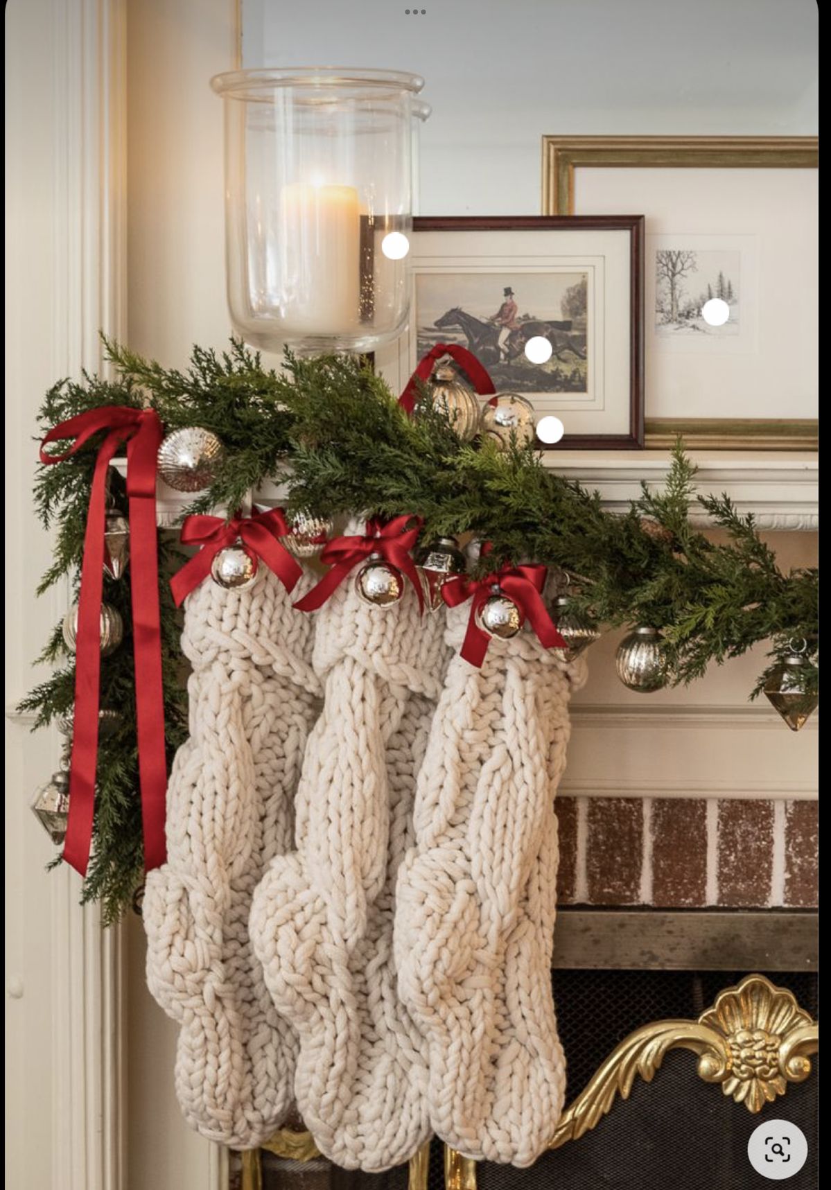 Christmas mantel decorated with chunky knit stockings, red ribbon bows, silver ornaments, and greenery garland.