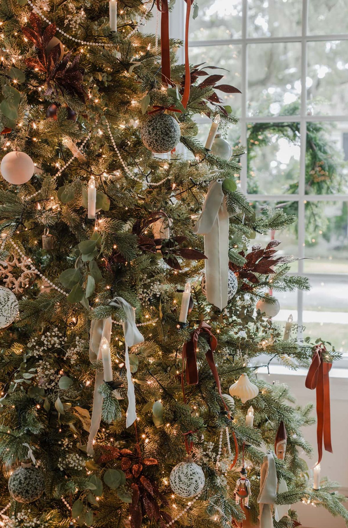 Christmas tree decorated with velvet ribbons in sage green and burgundy, white candles, and natural greenery for elegant holiday decor.