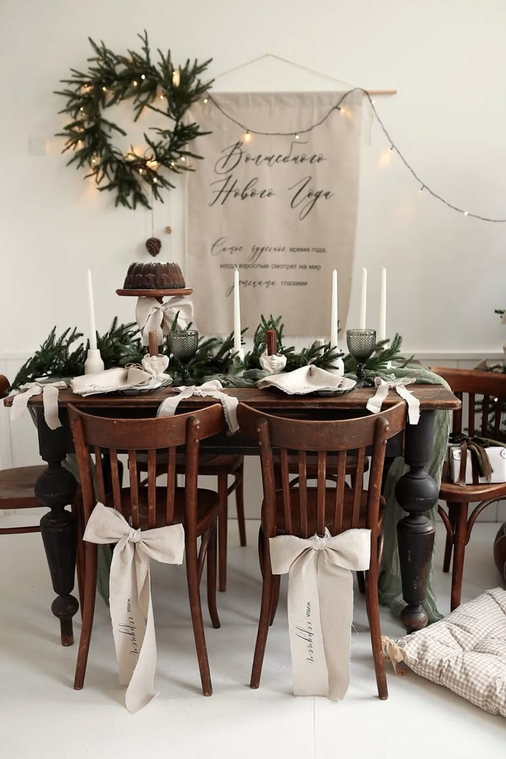 Rustic Christmas table decorated with neutral linen ribbons tied on chairs, greenery garland centerpiece, and white candles.