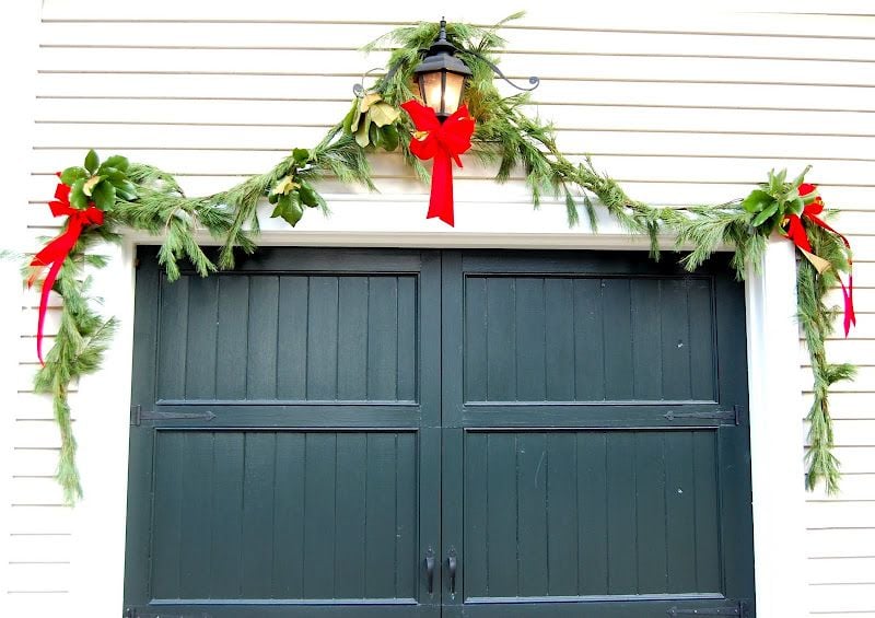 Green garage door decorated with natural garland and red bows for a classic Christmas look