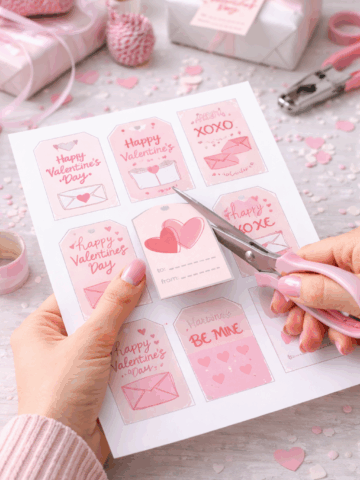 Woman’s hands cutting out free Valentine’s Day printable gift tags with scissors